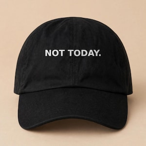 May include: A black baseball cap featuring the text NOT TODAY. embroidered in white capital letters across the front panels. The hat has a curved brim, a structured crown with a center seam, and a classic six-panel design with eyelets.