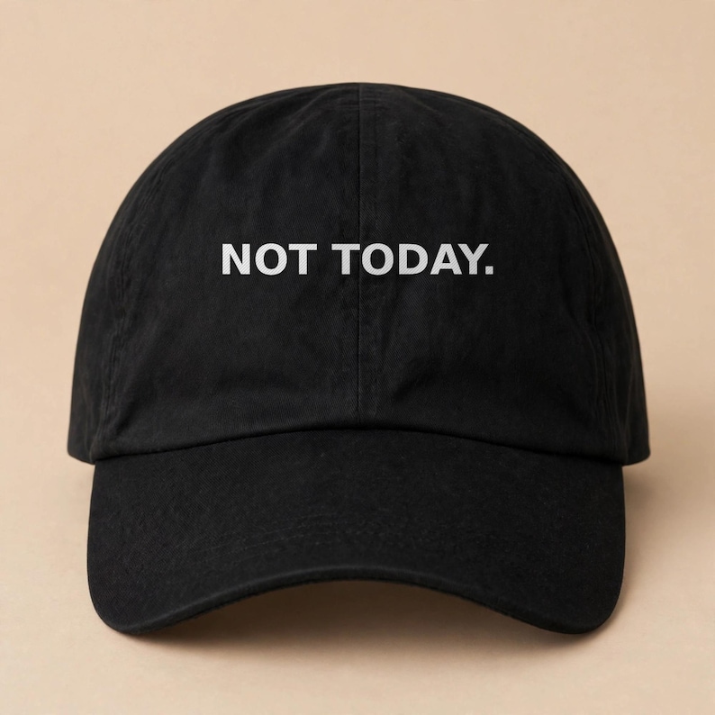 May include: A black baseball cap featuring the text NOT TODAY. embroidered in white capital letters across the front panels. The hat has a curved brim, a structured crown with a center seam, and a classic six-panel design with eyelets.
