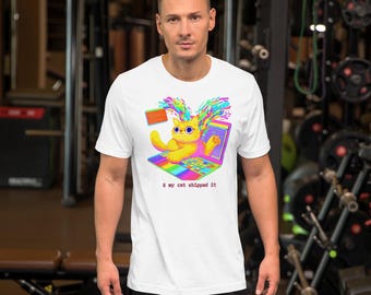 Pode incluir: Uma t-shirt branca de manga curta com o gráfico de um gato amarelo sentado num portátil colorido com salpicos de tinta arco-íris. O texto $ my cat shipped it está impresso a vermelho por baixo do gráfico do portátil.