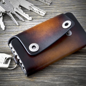 May include: A brown leather key holder with a flap closure and a metal ring. The key holder has a distressed look and two metal snaps.