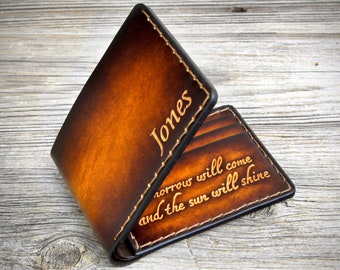 May include: A brown leather wallet with a stitched edge and gold lettering. The wallet is personalized with the name "Jones" and the quote "Tomorrow will come and the sun will shine".