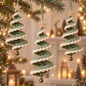 May include: Three spiral-shaped Christmas tree ornaments made of sage green crochet yarn with white scalloped edges. Each ornament features a small beige crocheted star at the top and a tiny metallic bell hanging from the bottom point.