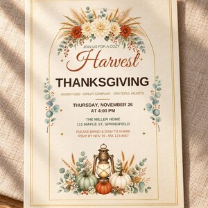 Op de afbeelding: Een rechthoekige Thanksgiving-uitnodigingskaart met een boogvormig kader versierd met bloemen- en tarweillustraties. De tekst bevat: Join us for a cozy Harvest Thanksgiving, Good Food, Great Company, Grateful Hearts, Thursday, November 26 at 4:00 PM, The Miller Home, 111 Maple St, Springfield, Please bring a dish to share, RSVP by Nov 19 - 555 123-4567. Onderaan staan een lantaarn en pompoenen.