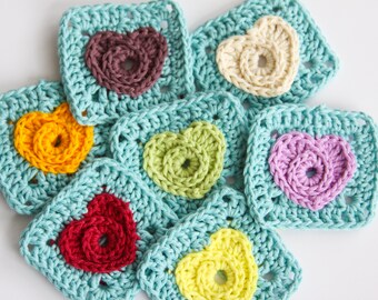 May include: Seven crocheted squares with different colored hearts in the center. The squares are turquoise blue and the hearts are brown, yellow, green, purple, red, and yellow.