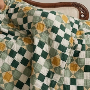 May include: A patchwork quilt featuring a repeating geometric pattern of squares and star motifs in shades of forest green, sage green, mustard yellow, and off-white. The textile is constructed from stitched fabric blocks with a finished border.