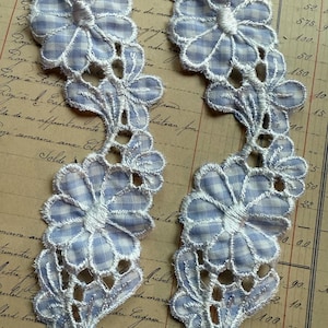 May include: Two floral appliques with a blue and white gingham pattern. The flowers are outlined with white stitching and have a delicate, openwork design. The appliques are on a vintage paper background.