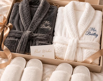 Op de afbeelding: Een geschenkdoos met een donkergrijze pluche badjas geborduurd met Mr. Bentley, een witte pluche badjas geborduurd met Mrs. Bentley en twee paar witte pluche slippers. Een kaartje met de tekst Best Wishes zit in de doos.