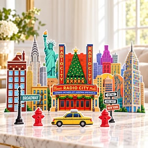 May include: A decorative New York City skyline display featuring the Statue of Liberty, Radio City Music Hall with a Christmas tree, a yellow taxi, fire hydrants, and street signs labeled Broadway, One Way, and New York.