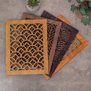 May include: A set of four rectangular wooden vent covers featuring intricate laser-cut patterns. The designs include repeating scalloped arches, a vertical leaf-like vein structure, a circular grid, and a geometric interlocking chain pattern.