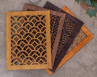 May include: A set of four rectangular wooden vent covers featuring intricate laser-cut patterns. The designs include repeating scalloped arches, a vertical leaf-like vein structure, a circular grid, and a geometric interlocking chain pattern.