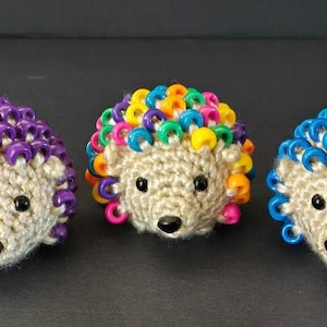 May include: Three crocheted hedgehogs with colorful plastic beads for quills. One hedgehog has purple beads, one has rainbow beads, and one has blue beads.