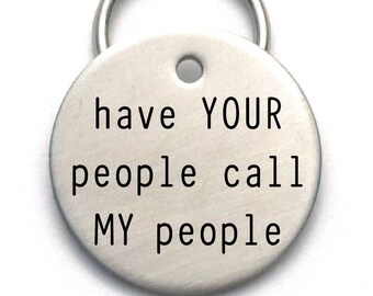 May include: Silver round dog tag with a key ring. The tag has the text "have YOUR people call MY people" engraved on it.