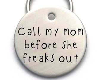 May include: Silver round dog tag with a key ring. The tag has the text "Call my mom before she freaks out" engraved on it.