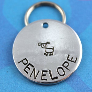May include: Silver dog tag with a hand-drawn dog and the name Penelope engraved on it.
