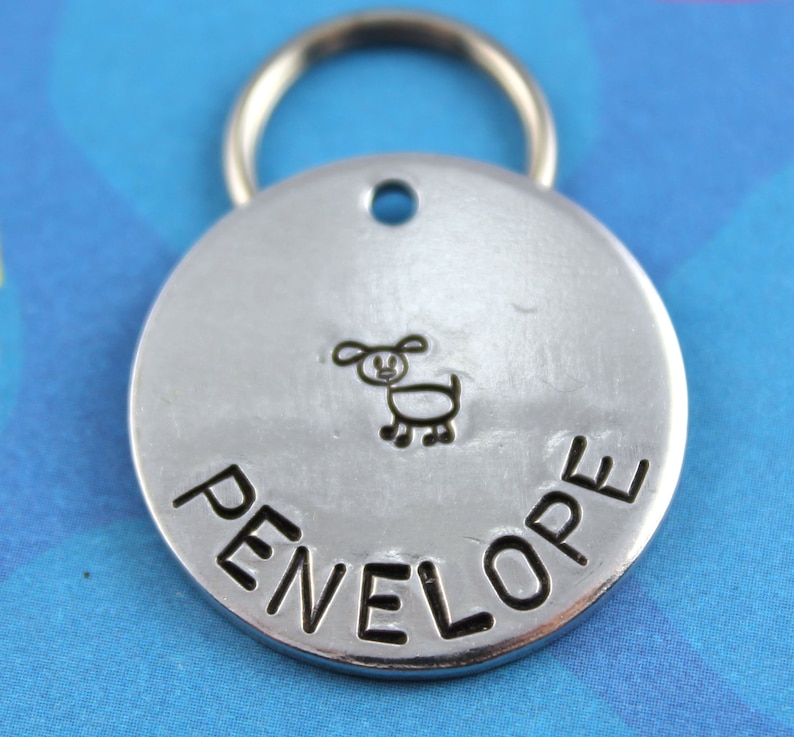 May include: Silver dog tag with a hand-drawn dog and the name Penelope engraved on it.