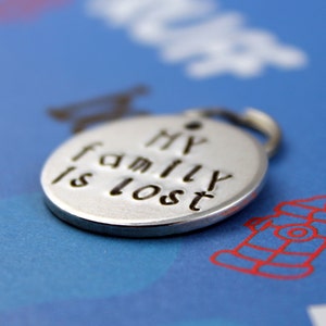 May include: A silver charm with the words "My family is lost" engraved on it. The charm is on a blue background with a red fire hydrant.