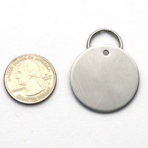 K&ouml;nnte beinhalten: Ein rundes, leeres Schild aus Silber mit einem Loch f&uuml;r einen Ring. Das Schild ist etwa so gro&szlig; wie eine US-amerikanische 25-Cent-M&uuml;nze.