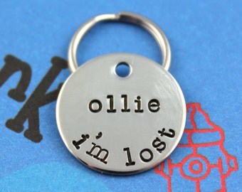 May include: Silver metal dog tag with a key ring. The tag has the text "ollie I'm lost" engraved on it.