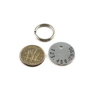 Puede incluir: Un llavero plateado con una etiqueta redonda plateada con los n&uacute;meros 123.456.7890 grabados en ella. Tambi&eacute;n se ve un llavero plateado y una moneda de diez centavos de d&oacute;lar estadounidense en la imagen.