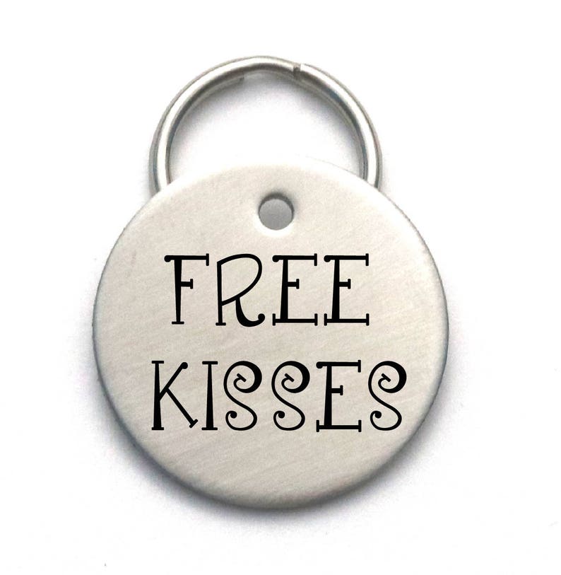 Op de afbeelding: Zilveren sleutelhanger met een rond label waarop in een decoratief lettertype "FREE KISSES" staat.