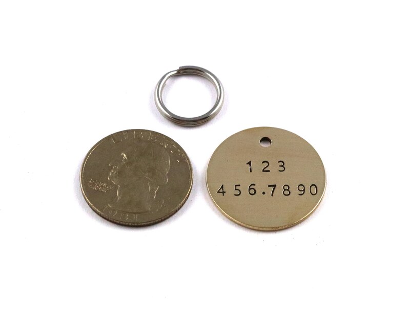 May include: A round brass tag with the numbers 123 456.7890 engraved on it. The tag is attached to a silver key ring.