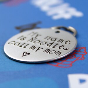 May include: Silver dog tag with the text "My name is Noodles, call my mom" and a small heart.