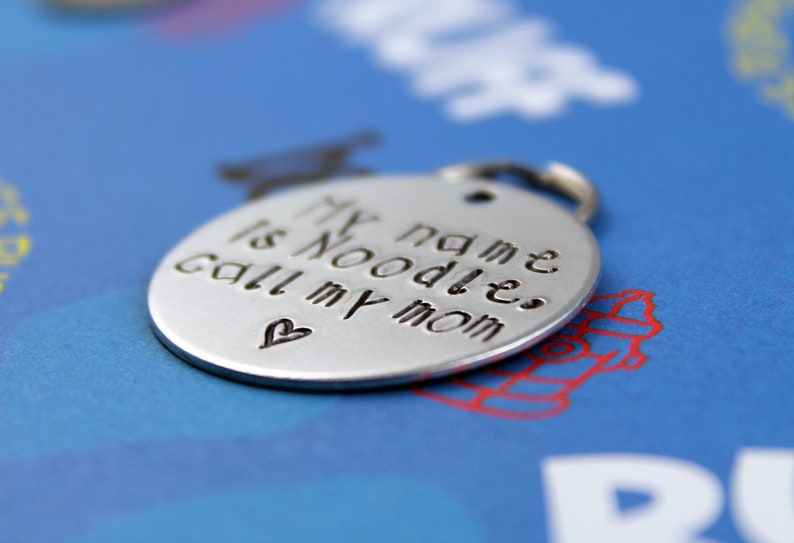 May include: Silver dog tag with the text "My name is Noodles, call my mom" and a small heart.