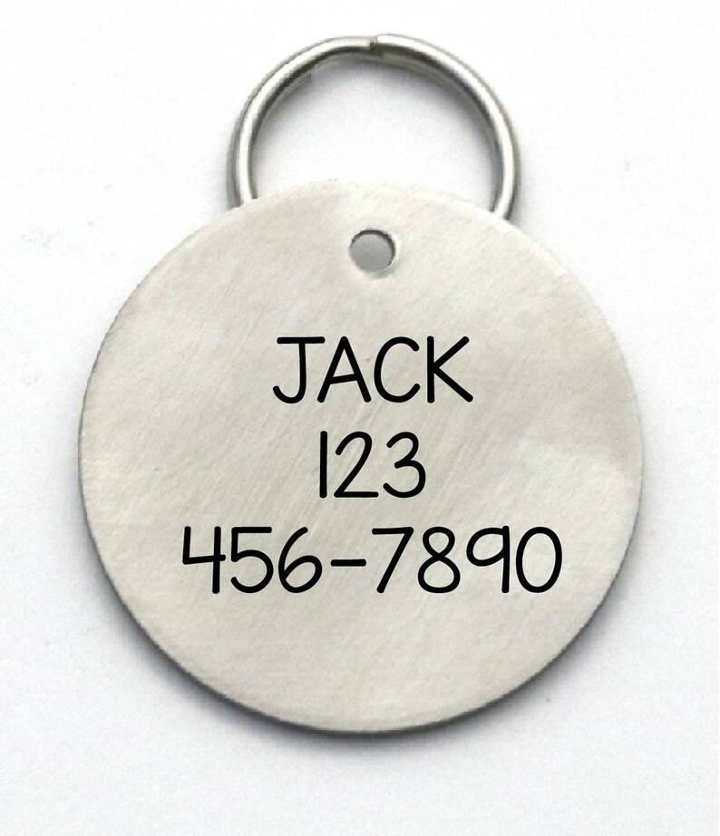 K&ouml;nnte beinhalten: Runder silberner Hundemarkenanh&auml;nger mit schwarzem Ring. Die Marke tr&auml;gt den Namen "JACK" und die Zahlen "123 456-7890" eingraviert.