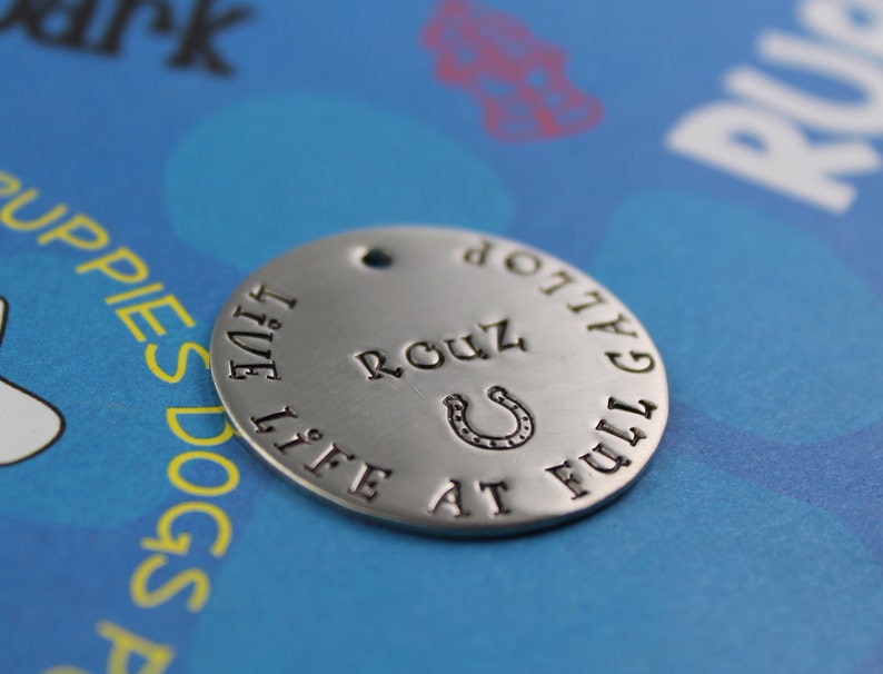 May include: Silver dog tag with the text "Live Life at Full Gallop" and a horseshoe with the name "Rouz" engraved on it.