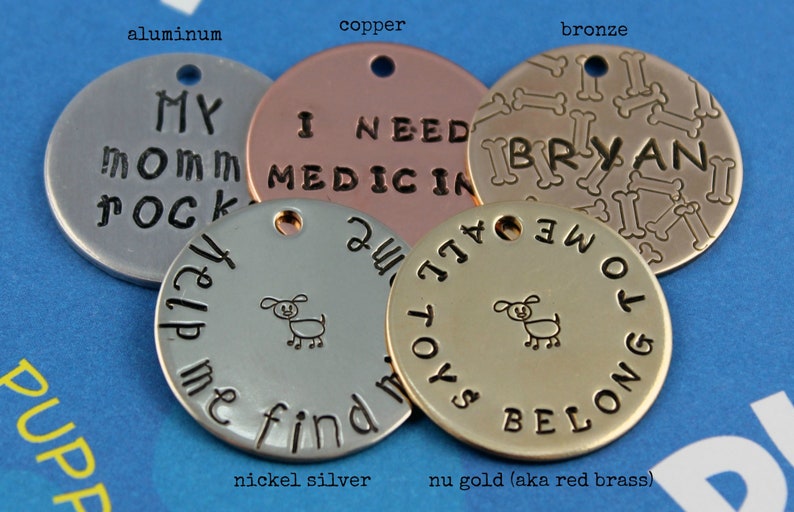 May include: Five round metal dog tags in different colors and finishes. The tags are engraved with various messages, including "My Mom Rocks", "I Need Medicine", "All Toys Belong To Me", and "Help Me Find My All Toys". The tags are also decorated with a small dog illustration and bone shapes.