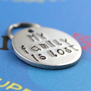 May include: Silver dog tag with the text "My family is lost" engraved on it.