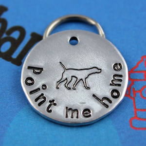 May include: Silver dog tag with a black silhouette of a dog and the text "point me home".