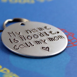 May include: Silver dog tag with the text "My name is Noodle. Call my mom" and a small heart.