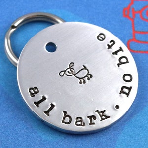 May include: Silver dog tag with a small dog illustration and the text "all bark no bite" engraved on it.