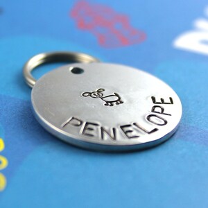 May include: Silver dog tag with a small dog illustration and the name "PENELOPE" engraved on it.