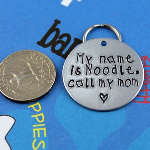 May include: Silver dog tag with a black inscription that reads "My name is Noodle. Call my mom" with a small heart symbol.