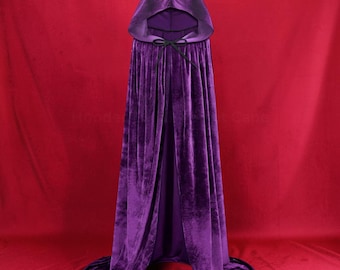 May include: A floor-length purple velvet cloak featuring a deep hood and a black tie closure at the neck. The fabric has a soft, reflective texture that drapes downward, creating a full silhouette with a rounded hemline at the base.