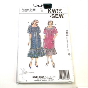 May include: A Kwik Sew pattern envelope 2485 for a square-neck dress with short sleeves and a ruffled hem. The illustration shows two variations: one in a blue patterned fabric and one in a solid pink fabric with patch pockets. Sizes S-M-L-XL-XXL.