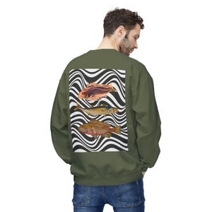 May include: An olive green crewneck sweatshirt featuring a rectangular graphic on the back. The graphic displays three distinct fish illustrations layered over a black and white wavy, distorted line pattern background.