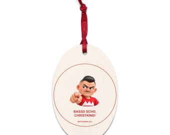 May include: An oval-shaped wooden ornament with a red ribbon hanger. It features a cartoon character pointing forward, wearing a red shirt with a white chevron. The text reads "BASSD SCHO, CHRISTKIND!" and "WUTFRANKE OLLI" in red.