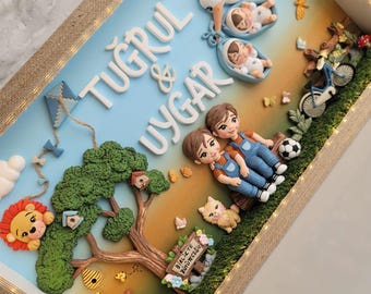 Puede incluir: Una caja de sombra con los nombres TUĞRUL & UYGAR en letras blancas. La escena incluye una cigüeña con dos bebés, dos niños sentados en un tronco, un árbol, una bicicleta, un león y un letrero que dice BIRLIKTE BÜYÜYECEĞIZ.