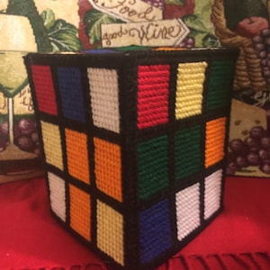 Könnte beinhalten: Ein Tissuebox-Bezug aus buntem Garn, der einem Rubik's Cube ähnelt. Der Bezug ist aus schwarzem, weißem, rotem, orangefarbenem, gelbem, grünem und blauem Garn.