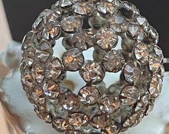 May include: A silver-toned, round, decorative piece with a sphere shape, covered in small, clear rhinestones.