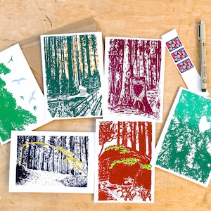 May include: Six different cards with illustrations of a forest. Each card has a different color scheme, including green, blue, red, and purple. The cards are arranged in a semi-circle on a wooden surface.