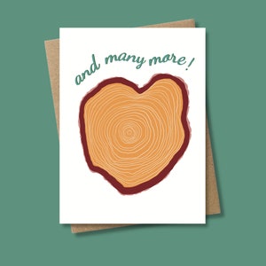 May include: A white card with a brown envelope. The card has a heart-shaped tree ring design with the text "and many more!" in green.