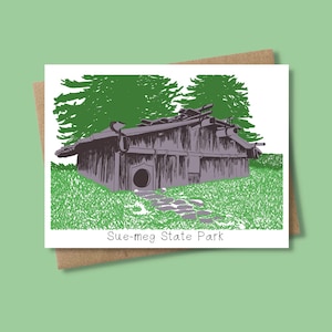 May include: A greeting card featuring a detailed illustration of a building at Sue-meg State Park. The building is depicted in shades of gray and purple, with a stone path leading to the entrance. The card is set against a green background, with the text "Sue-meg State Park" at the bottom.