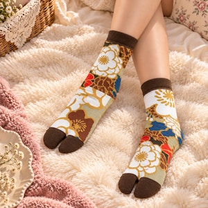 May include: A pair of split-toe tabi socks featuring a dark brown cuff and toe section. The socks are decorated with a vibrant floral pattern in shades of white, gold, red, and blue against a light background, showcasing a distinct separation for the big toe.