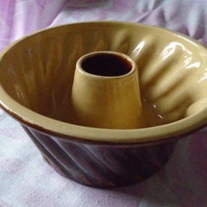 Pode incluir: Uma forma de bolo bundt de cerâmica marrom e bege com um design canelado. A forma tem um tubo central para assar um bolo em forma de anel.