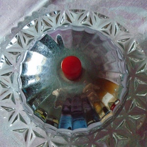 May include: A clear glass lid with a starburst pattern around the edge. The lid has a red knob in the center.