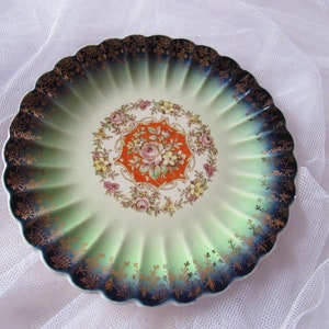 May include: A vintage porcelain plate with a scalloped edge and a green and blue ombre design. The center features a floral pattern with a red and orange accent.